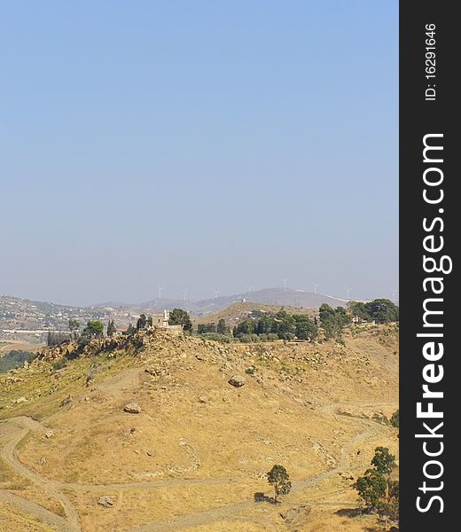 Vertical rural landscape, with house on the hilltop and modern windmills in the background; *with space for text (copyspace)