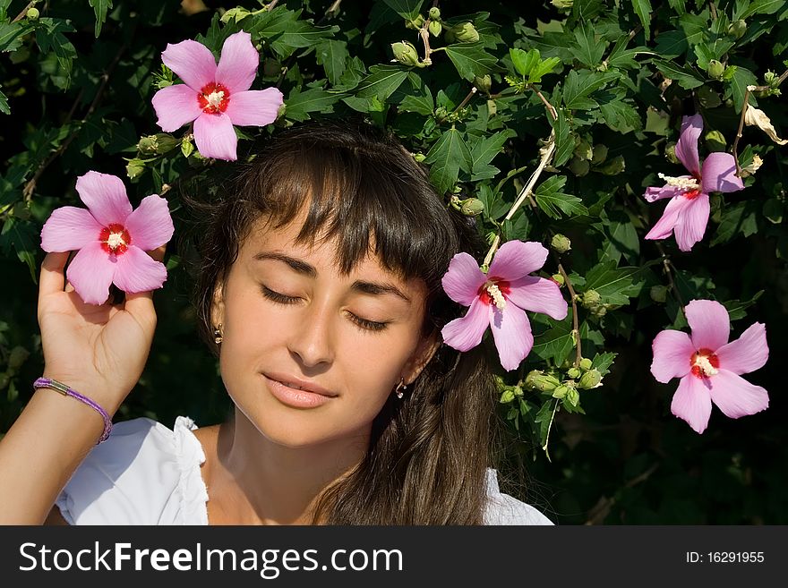 Young attractive girl enjoying blossoming of beautiful pink flowers and relaxing in the park. Young attractive girl enjoying blossoming of beautiful pink flowers and relaxing in the park