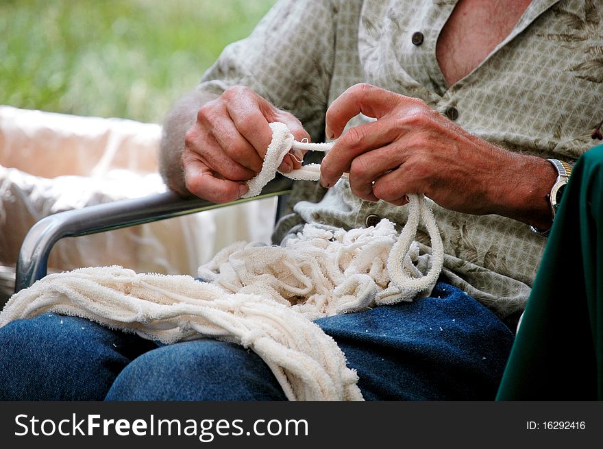 Elderly gentleman weaving strings of material for macrame art. Elderly gentleman weaving strings of material for macrame art.