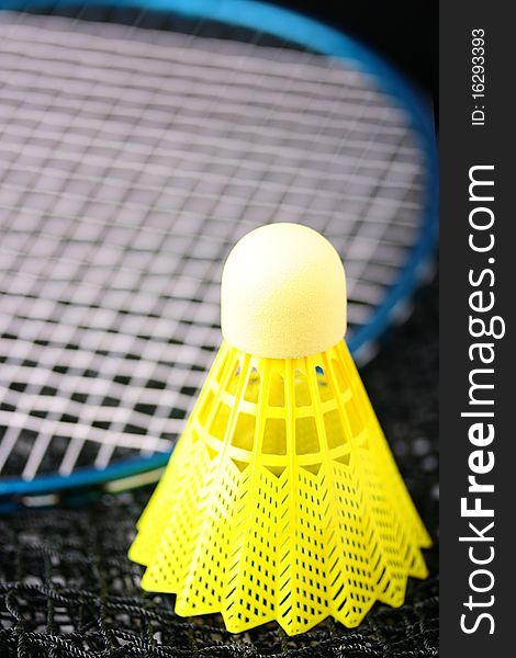 Bright yellow badminton shuttlecock and blue racquet laying on a badminton net. Bright yellow badminton shuttlecock and blue racquet laying on a badminton net.
