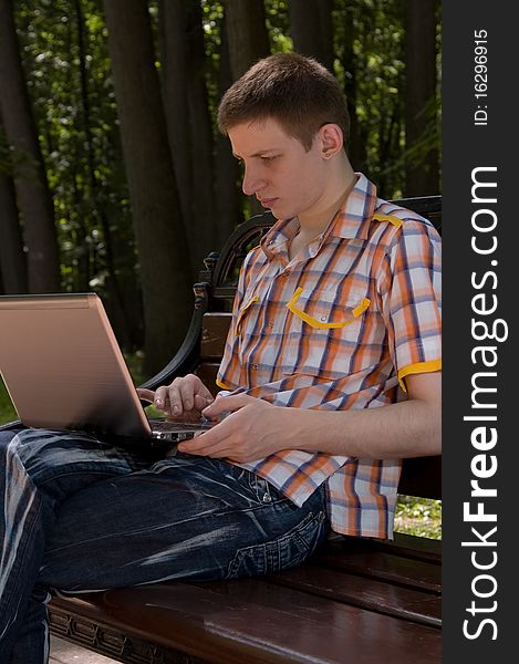 Young man sitting on a bench  in green park and types on laptop. Young man sitting on a bench  in green park and types on laptop