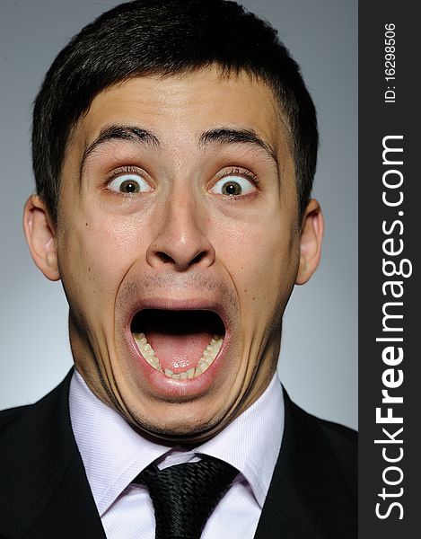 Portrait of stressed business man in formal suit and black tie screaming. gray background