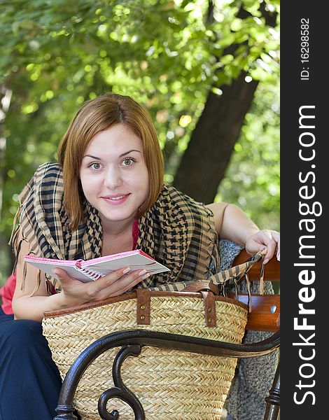Red-haired woman sitting on a bench with book and smilling at the camera. Red-haired woman sitting on a bench with book and smilling at the camera