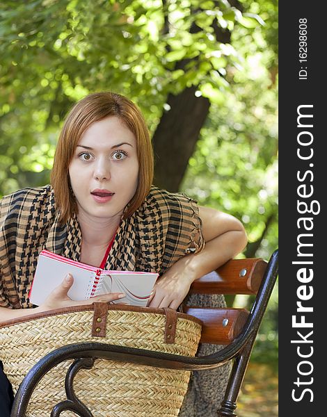 Beautiful red-haired woman reading and looking surprised on a bench