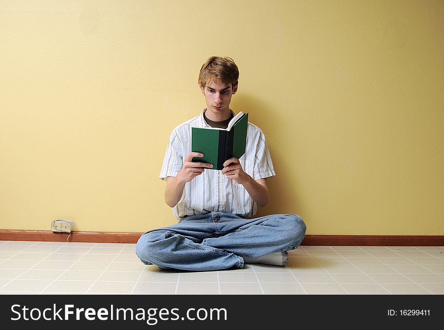 A young male reading a small hardcover book in an empty room with lots of copyspace around his body. A young male reading a small hardcover book in an empty room with lots of copyspace around his body.