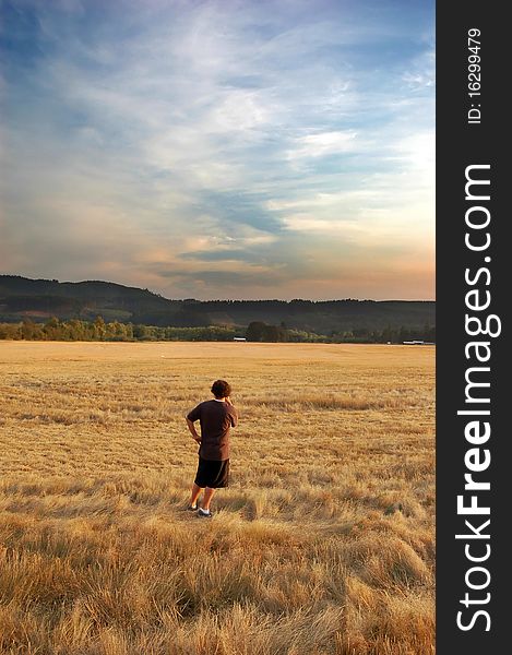 A young adult looking at beautiful wheat farm land in a rural country field with a golden sunset and mountains on the horizon. Copyspace above in the sky with room for your text. A young adult looking at beautiful wheat farm land in a rural country field with a golden sunset and mountains on the horizon. Copyspace above in the sky with room for your text.