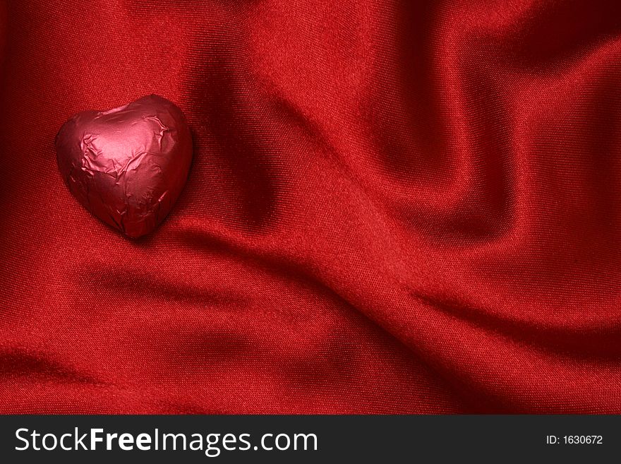 Red heart shaped foiled chocolate on red satin. Red heart shaped foiled chocolate on red satin