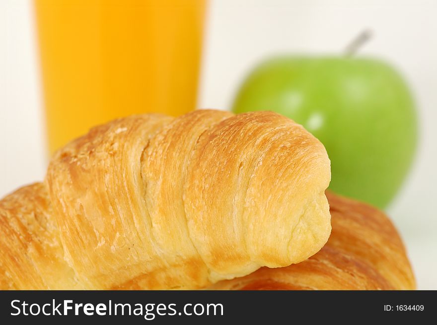 Fresh-baked croissant, orange juice and green apple.  Shallow DOF. Focus on croissant. Fresh-baked croissant, orange juice and green apple.  Shallow DOF. Focus on croissant.