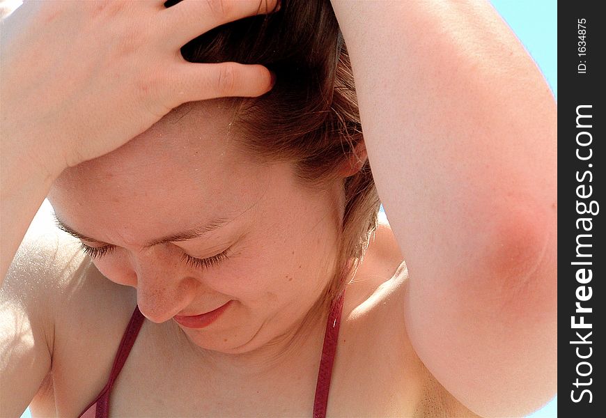 A closeup of a young woman puller her hair away from her face while looking down. A closeup of a young woman puller her hair away from her face while looking down