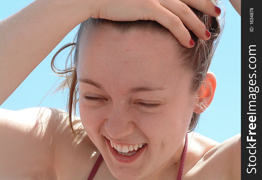 A closeup of a young woman pulling her hair away from her face while laughing. A closeup of a young woman pulling her hair away from her face while laughing