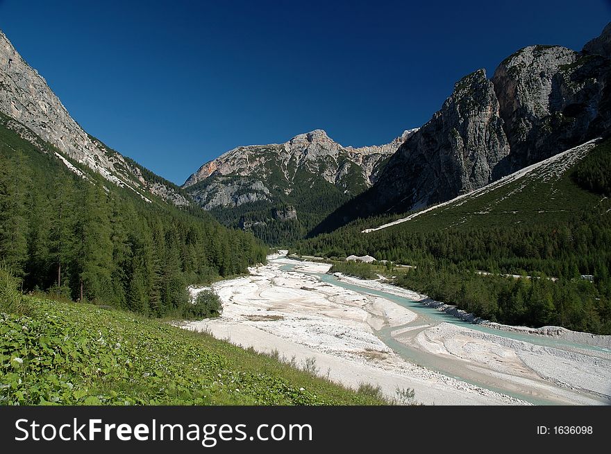 Mountain river with wide riverbed with Dolomiti mountains in Italy in background.