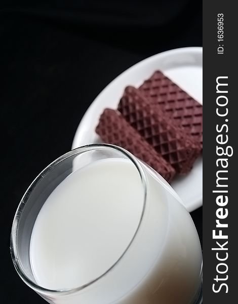 Chocolate cookies and milk over black background