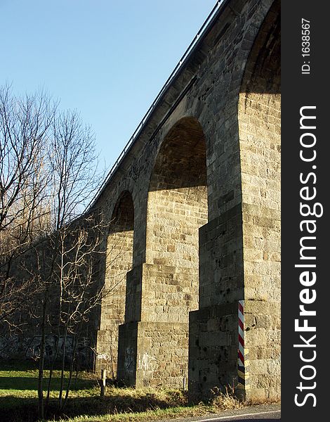 Very old stone bridge with three arch supports and a road passing through one arch. Very old stone bridge with three arch supports and a road passing through one arch.