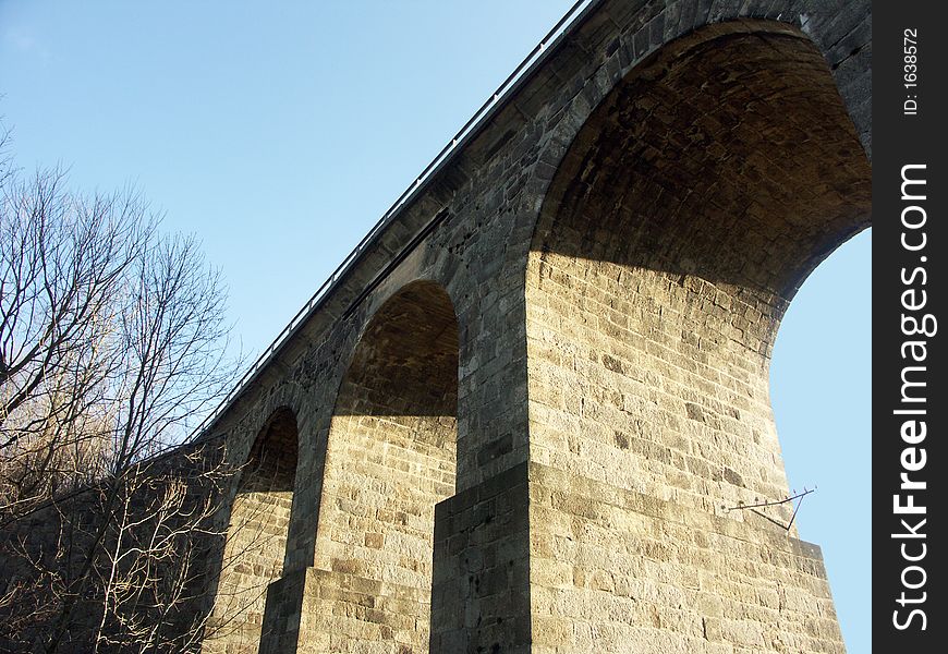 Very old stone bridge with three arch supports and a road passing through one arch. Very old stone bridge with three arch supports and a road passing through one arch.