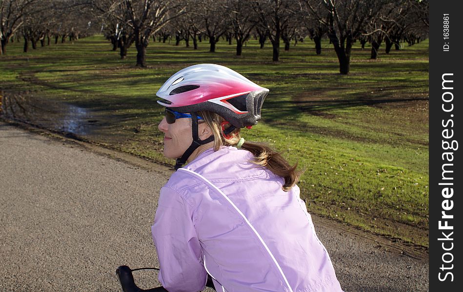 Woman on bike smiling and leaning on handlebars in lavendar jacket stopped by an almond orchard. Woman on bike smiling and leaning on handlebars in lavendar jacket stopped by an almond orchard.