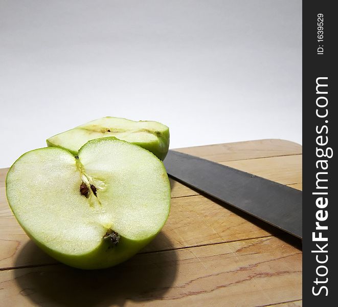 Photo of a green apple on a cutting board after being sliced in half with the knife next to it. Photo of a green apple on a cutting board after being sliced in half with the knife next to it