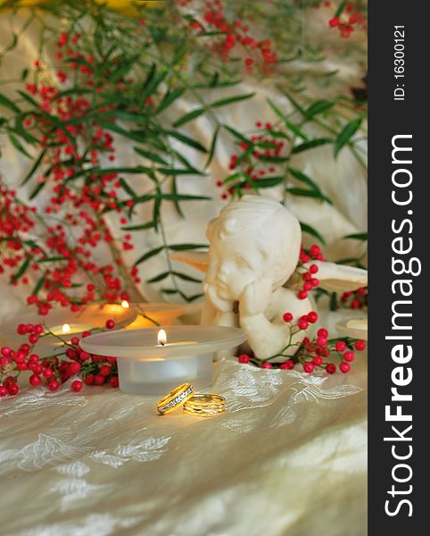 Gold wedding rings with pinkish berries, greenery, angle and candles on ivory silk. Gold wedding rings with pinkish berries, greenery, angle and candles on ivory silk