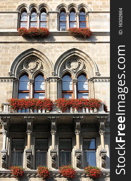 Old style windows with red flowers, on a mainson facade.