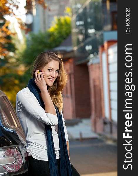 Beautiful blond female on the phone reclined against the car outdoors. Beautiful blond female on the phone reclined against the car outdoors