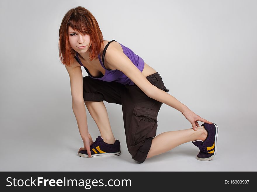 Young redhead girl in hip-hop clothes sitting on one knee and looking at camera, full body