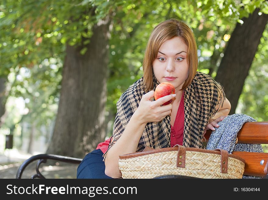 Red-haired woman sitting on a bench and looking at apple. Red-haired woman sitting on a bench and looking at apple
