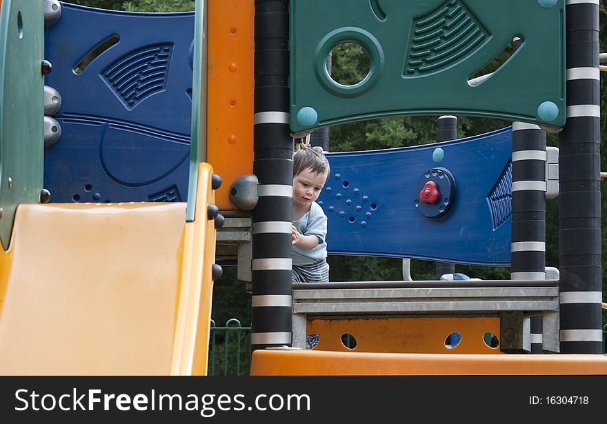 A small child playing in a children outdoor playground with modern equipment of climbing frame and slide. A small child playing in a children outdoor playground with modern equipment of climbing frame and slide.