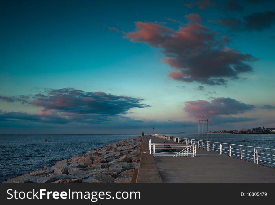 A breakwater at sunrise, with big dark clouds in the sky.