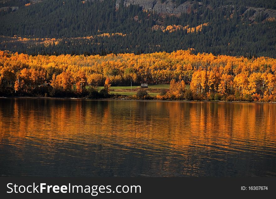 Cottage sits nestled in autumn trees beneath mountain. Cottage sits nestled in autumn trees beneath mountain