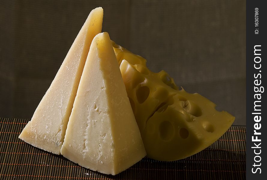 Three pieces of italian and swiss cheeses over brown background. Three pieces of italian and swiss cheeses over brown background