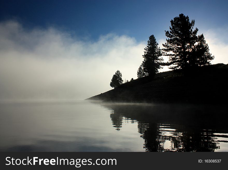 Fog lifts from the lake to reveal shore. Fog lifts from the lake to reveal shore