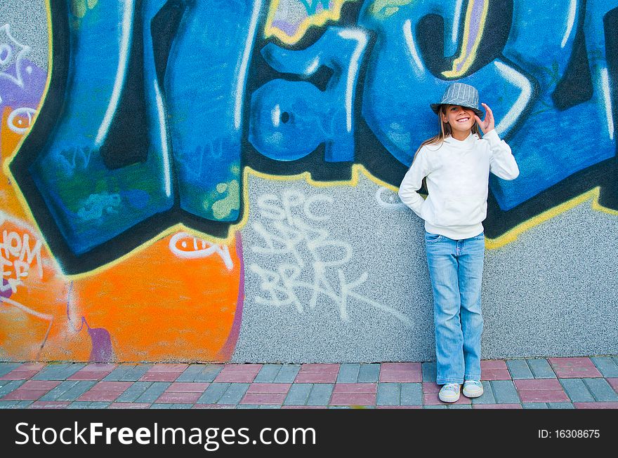 Fashionable stylish beautiful girl standing near a wall with graffiti. Outside. Fashionable stylish beautiful girl standing near a wall with graffiti. Outside