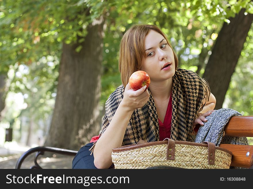 Redheaded woman sitting on bench and looking at apple. Redheaded woman sitting on bench and looking at apple