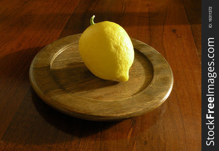 Photograph of a lemon perched on a round plate of wood, which in turn rests on a wooden table. Photograph of a lemon perched on a round plate of wood, which in turn rests on a wooden table.