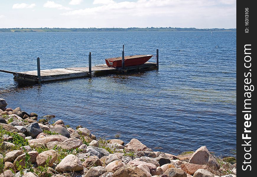 Small wooden jetty dock with a dingy boat sea ocean background