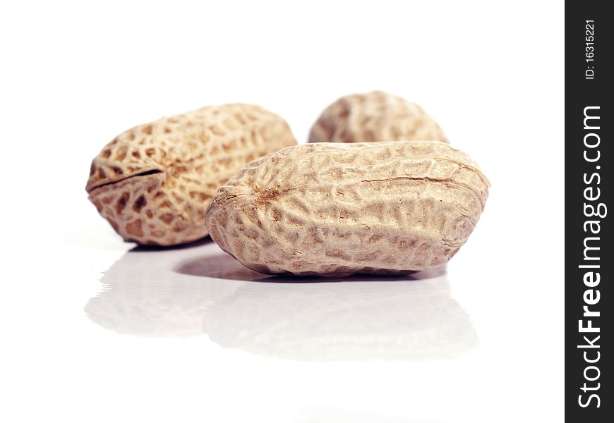 Three unshelled peanuts, isolated on white with reflection. Shallow depth of field with the nearest nut in focus.