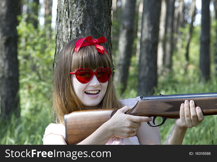Girl with heart-shaped sunglasses holding a rifle in the forest. Girl with heart-shaped sunglasses holding a rifle in the forest