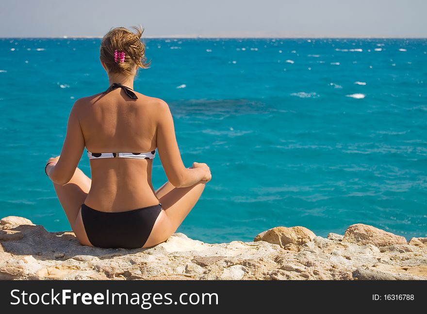 Woman in a sarong meditating on the beach