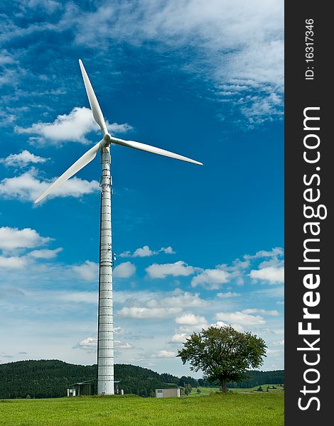 A wind wheel in front of a blue, overcast sky. In the foreground a meadow. A wind wheel in front of a blue, overcast sky. In the foreground a meadow