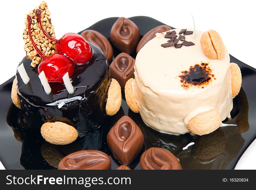 Cake with white and dark chocolate and chocolates on the black plate isolated on a white background.