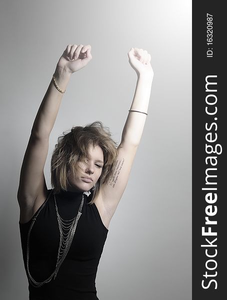 Young stylish woman in dark clothing and jewelry on her neck and hands, with a calm and somewhat aloof expression on his face, stretched his arms raised high up. Young stylish woman in dark clothing and jewelry on her neck and hands, with a calm and somewhat aloof expression on his face, stretched his arms raised high up.