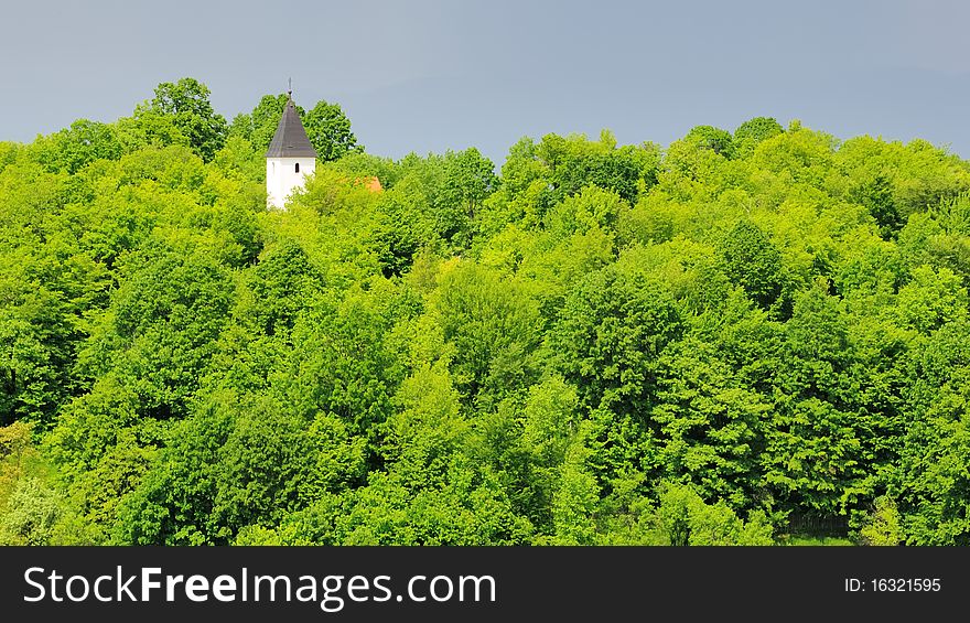 Small church with white tower in a dense  forest in spring with a thunderstorm in the background. Small church with white tower in a dense  forest in spring with a thunderstorm in the background