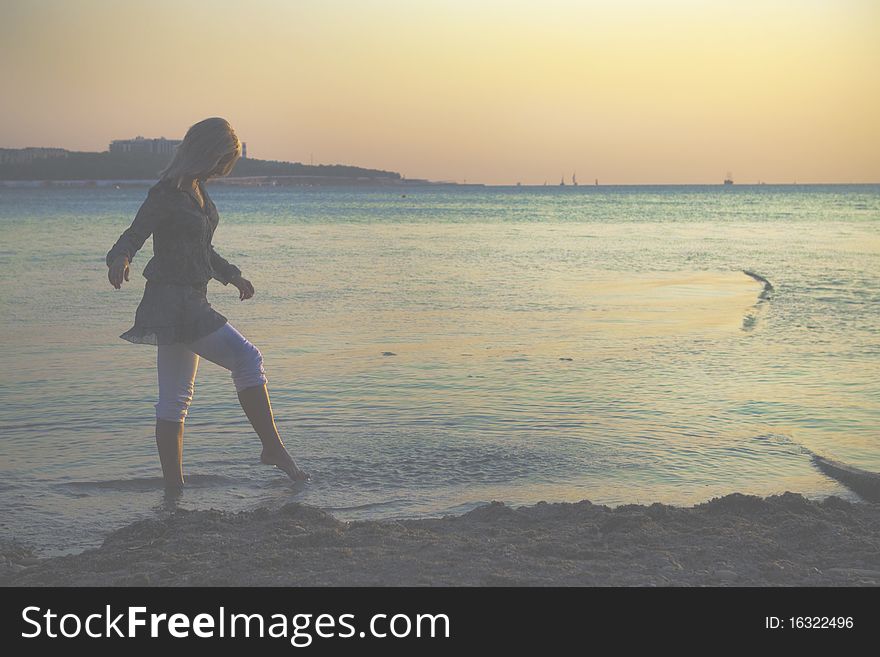 At sunset, the girl walks on the beach