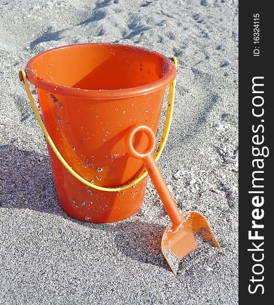 Orange bucket and shovel resting on the sandy beach