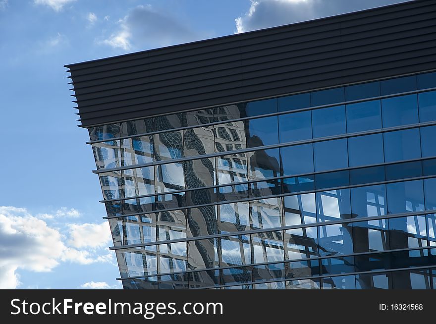 The corner of of a glass building. The blue sky with cloud in the background. The corner of of a glass building. The blue sky with cloud in the background.