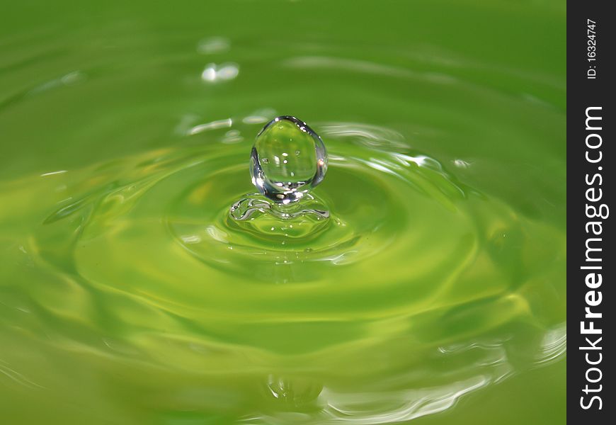 The green drop of water falls leaving circles on a surface being reflected and sparkling. The green drop of water falls leaving circles on a surface being reflected and sparkling