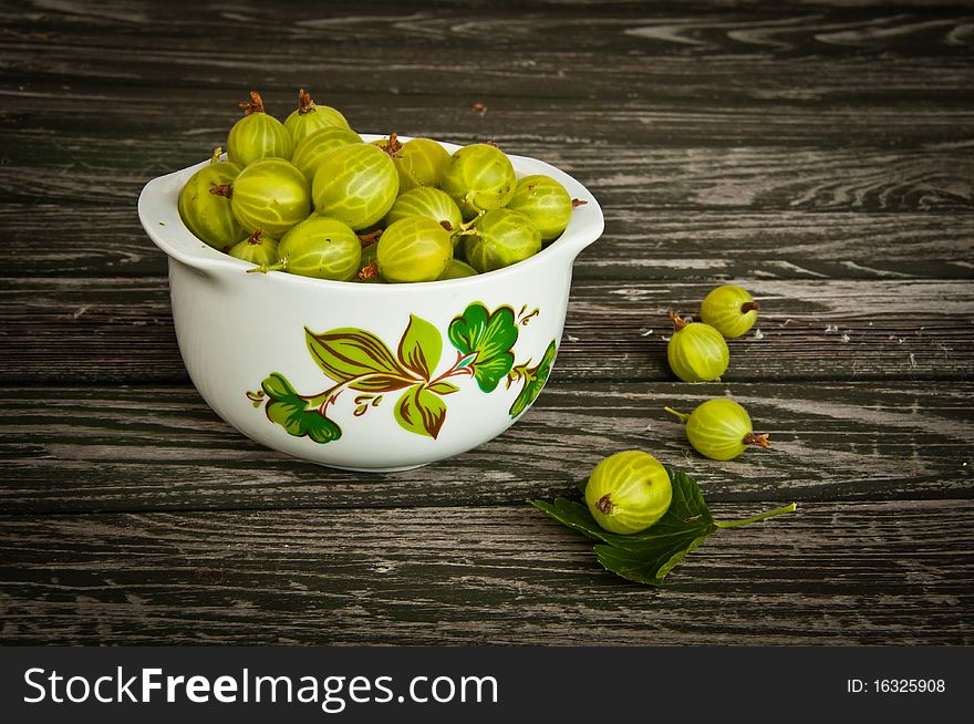 Flower-decorated bowl of freshly picked gooseberries on wooden garden table