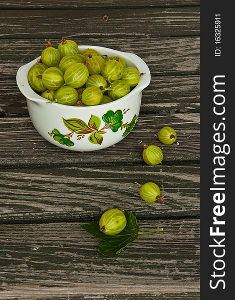 Flower-decorated bowl of freshly picked gooseberries on wooden garden table