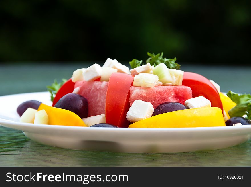 Plate of fresh summer salad with tomeaotes, watermelon, bell peppers, grapes, feta cheese and cucumber