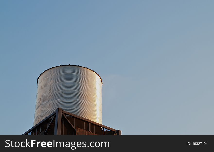 Brightly late sun lit steel water tank on tower against clear blue sky. Brightly late sun lit steel water tank on tower against clear blue sky