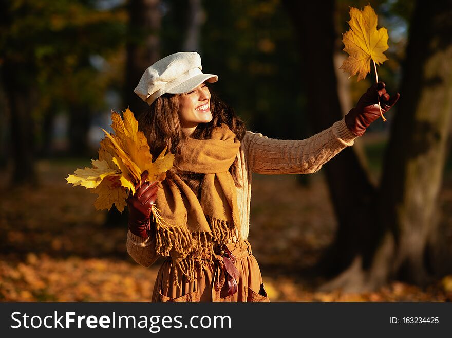 Happy woman outside in autumn park looking at yellow leaf
